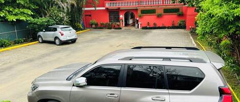 A beige SUV parked in front of a red building with a balcony.
