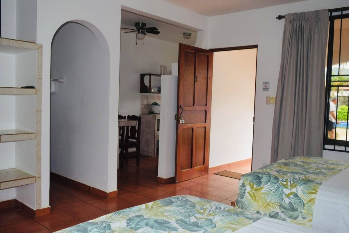 A room with a bed, a desk, and a kitchenette.