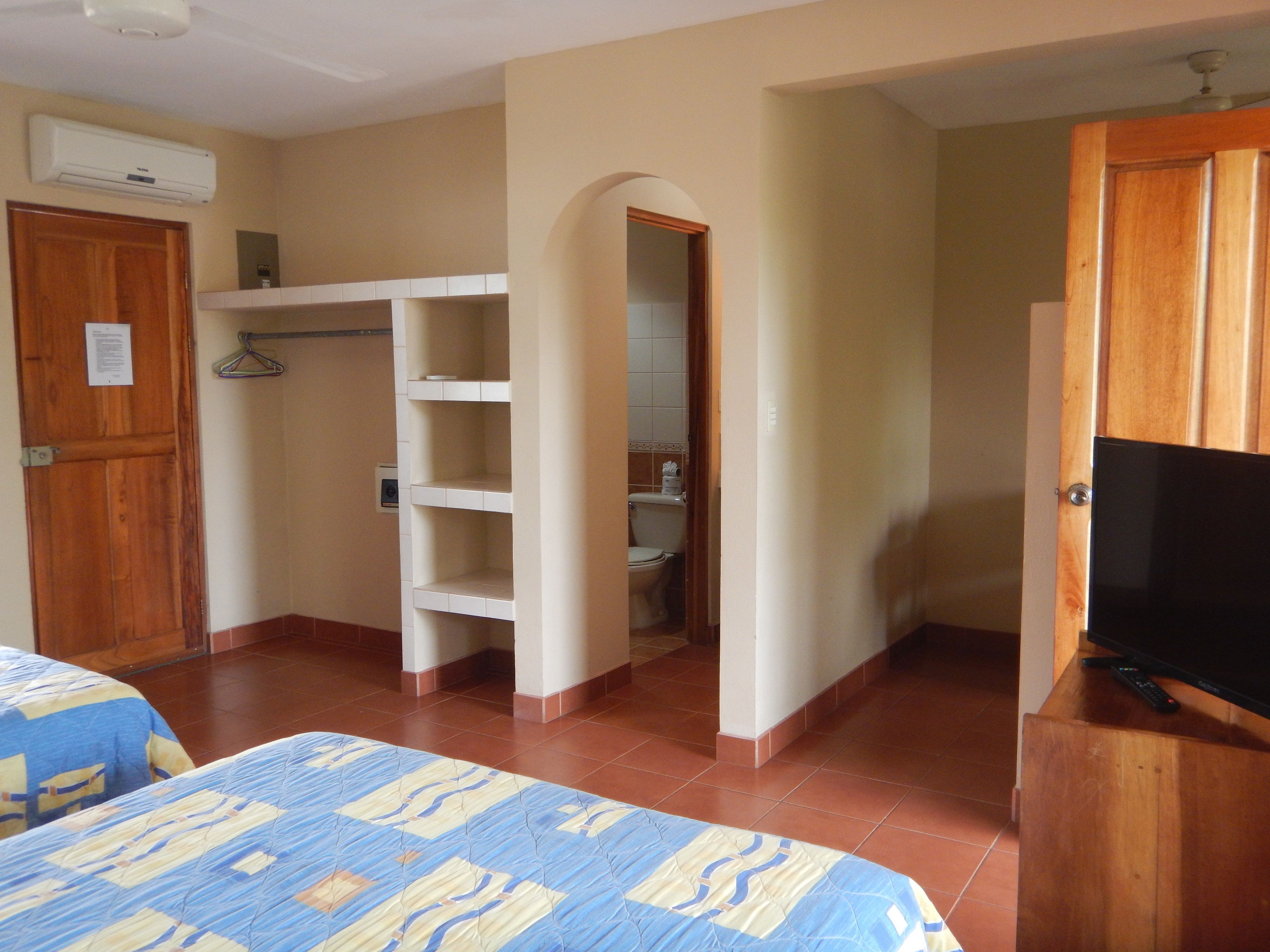 A hotel room with a bed, a TV, a wardrobe, and a bathroom visible through an archway.