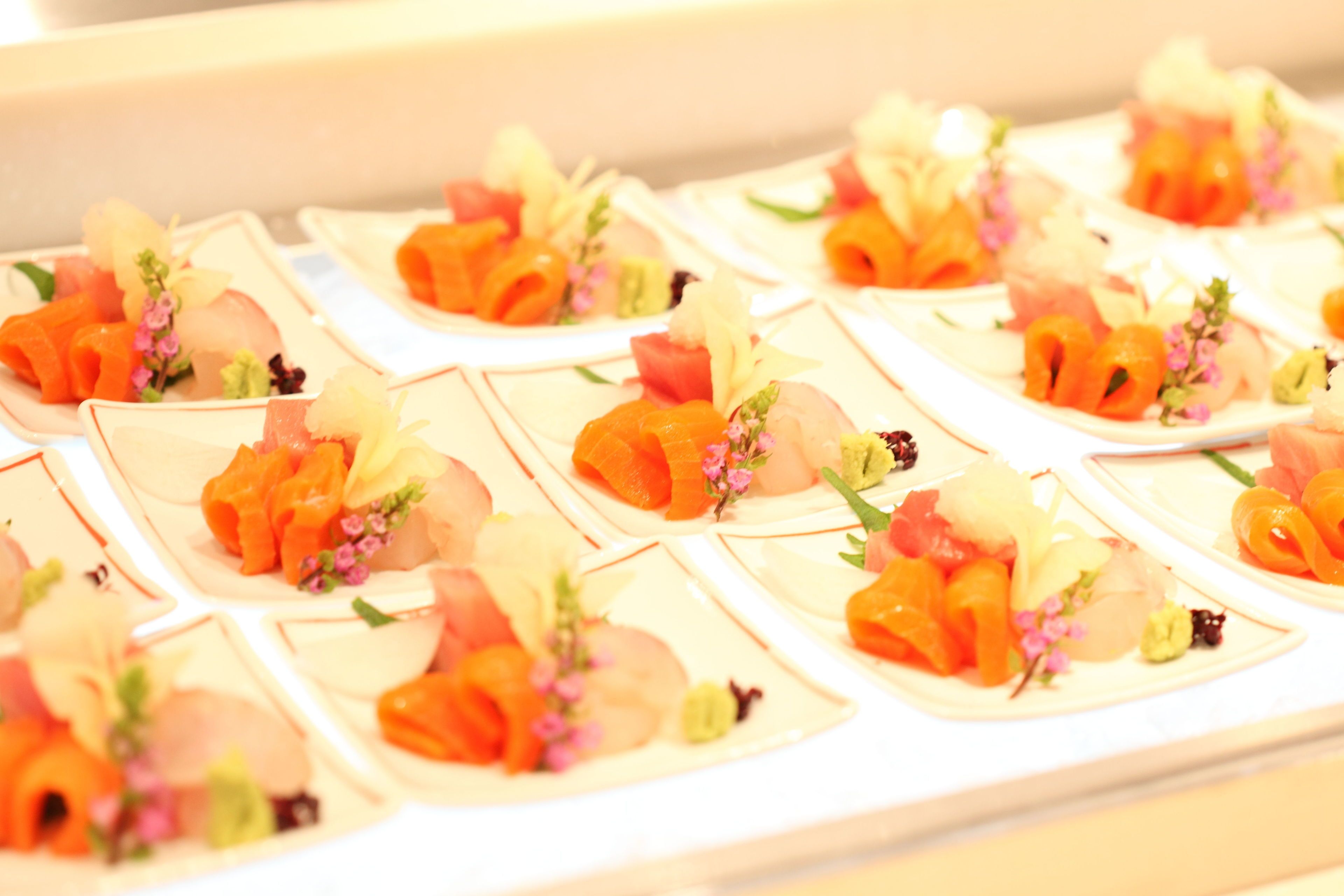 Presentación de pequeños bocados de sushi sobre platos cuadrados, cada uno decorado con flores y verduras.