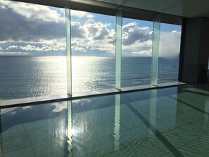 Amplio espacio interior con grandes ventanales que dan a una masa de agua y un cielo despejado.