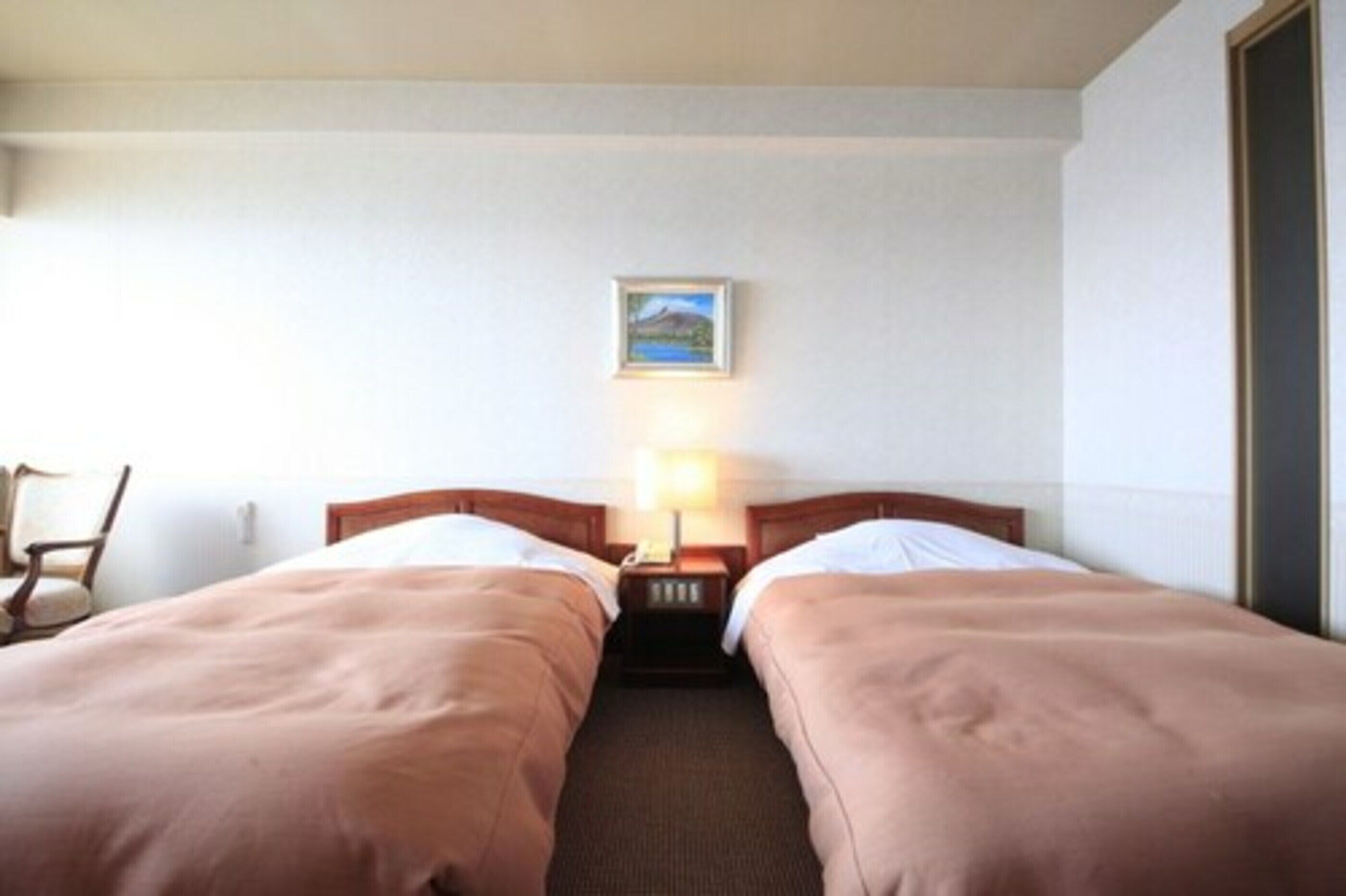 Ein Hotelzimmer mit zwei Einzelbetten, einem Nachttisch mit Lampe, einem Sessel und einem gerahmten Bild an der Wand.
