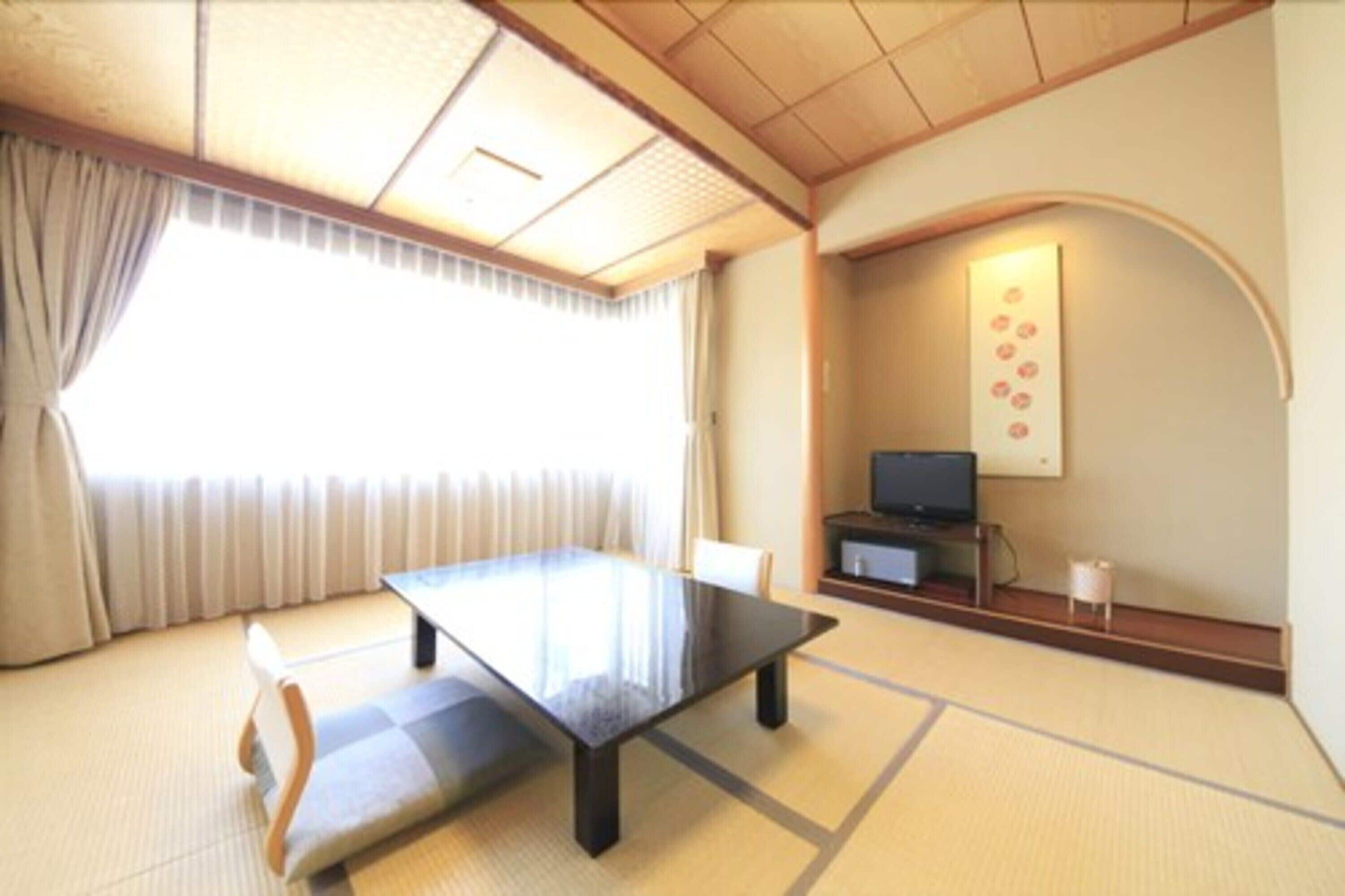 Una habitación japonesa tradicional con suelo de tatami, una mesa baja, un televisor y una obra de arte colgada en la pared.