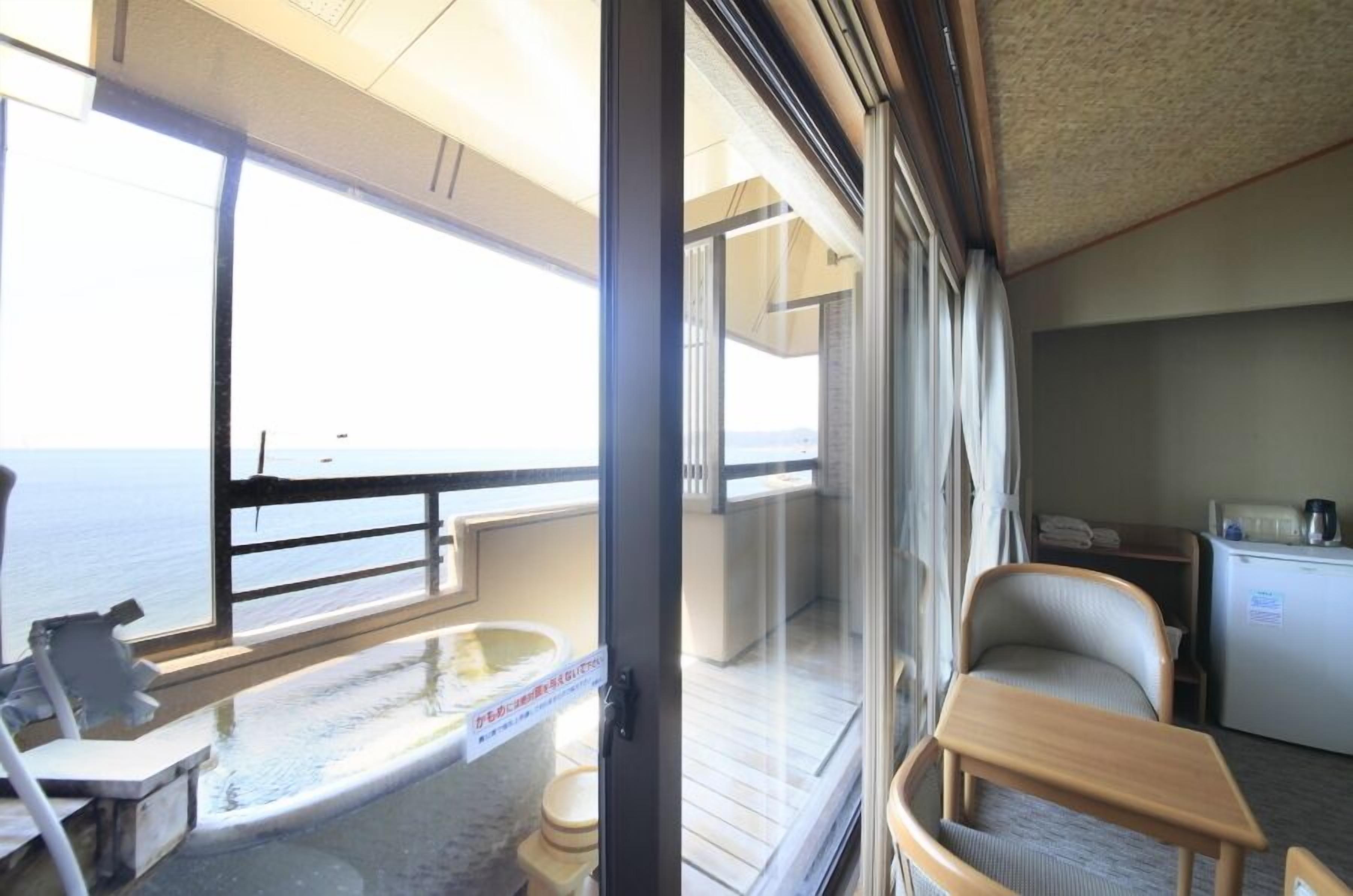 A balcony with a view of the sea, a small table, a chair, and a refrigerator.
