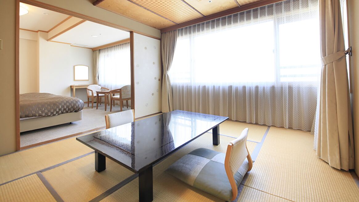 A traditional Japanese room with tatami flooring, a low table, a sofa, and a desk with chairs.