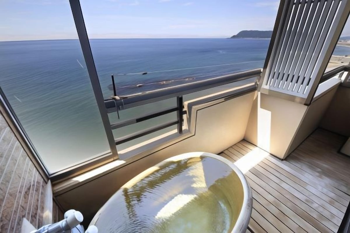 A balcony with a glass-enclosed jacuzzi, a wooden deck, and a view of the sea.