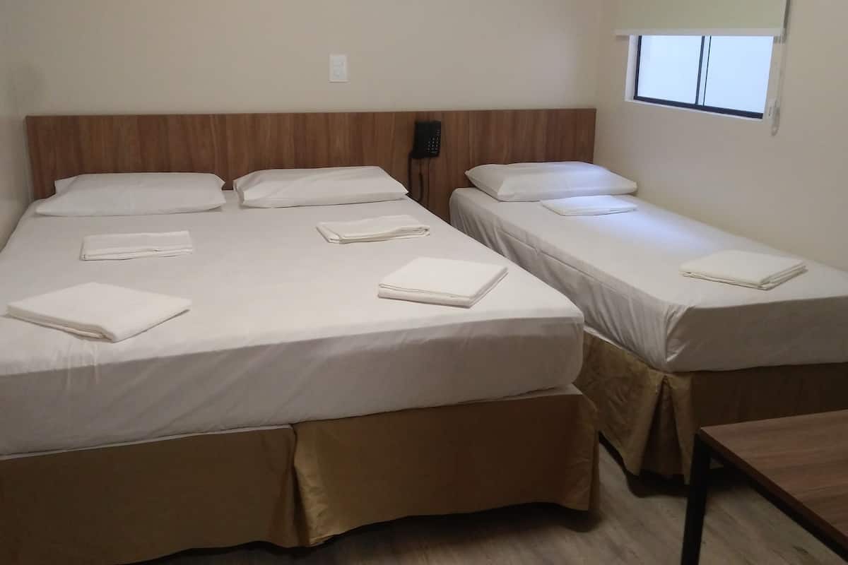 Hotellihuone, jossa on kaksi sänkyä. Jokaisessa sängyssä on valkoiset lakanat ja tyynyt, puinen pääty sekä puhelin yöpöydällä ja pieni ikkuna.