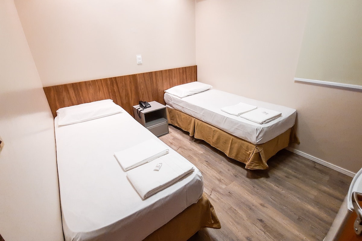 Pieni hotellihuone, jossa on kaksi erillistä sänkyä, puinen pääty, yöpöytä, jossa on puhelin, ja seinälle asennettu ilmastointilaite.