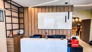 A modern reception desk with a large screen, wooden paneling, and a clock on the left. - Hub Hotel (Teresina)
