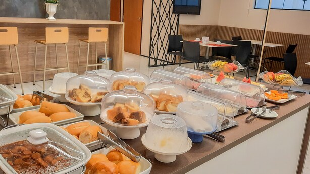 A buffet with various food items, a seating area with chairs, a television, and a plant. - Hub Hotel (Teresina)