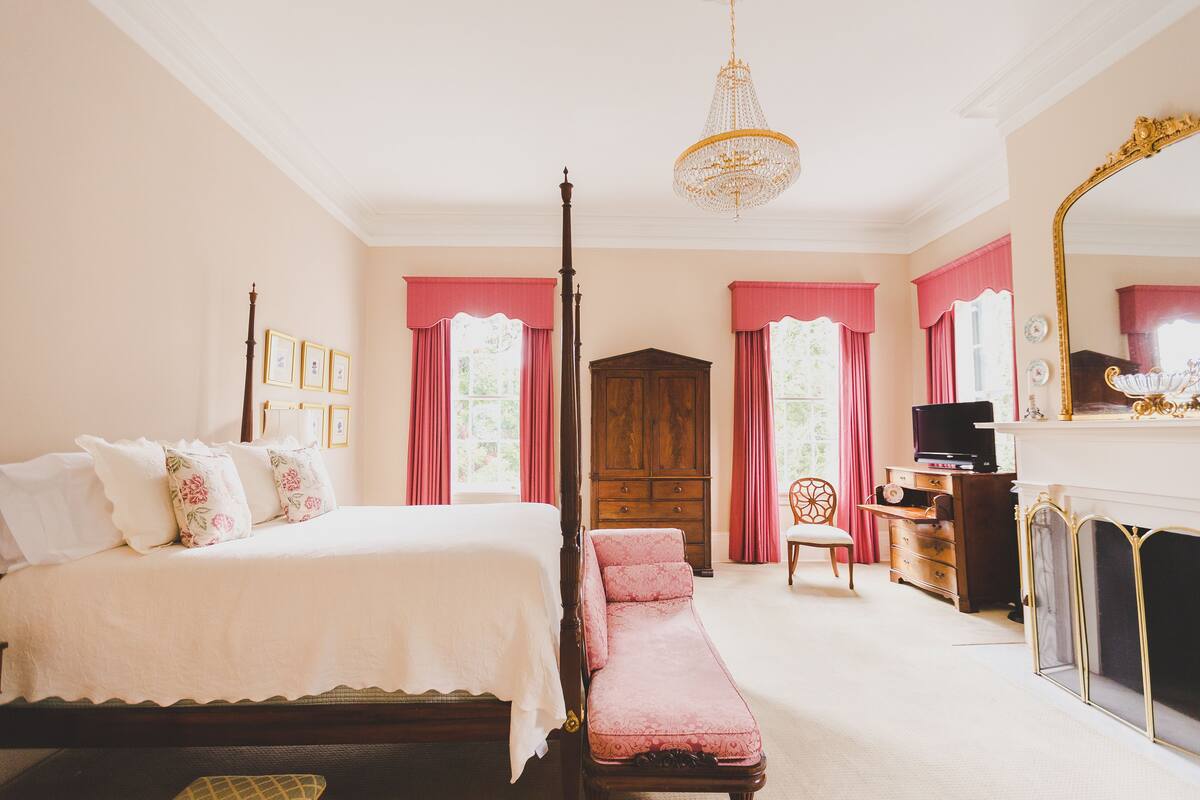 Un dormitorio con cama con dosel, un chaise lounge, un armario de madera, un televisor y una chimenea.