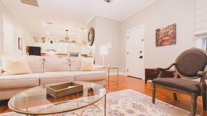 A living room with a sofa, a glass coffee table, a patterned rug, a wooden chair, and a kitchen in the background. - Brandon Hall Plantation (Natchez)