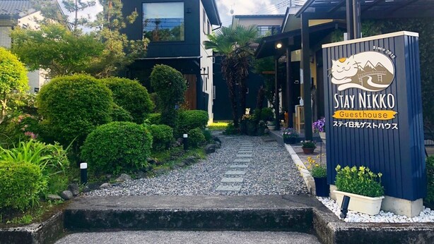 A modern guesthouse with a well-maintained garden, a clear pathway, and a signboard indicating the name 'STAY NIKKO'.