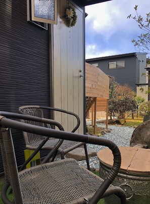 A wicker chair and a table outside a building with a dark brick wall and a wooden door.