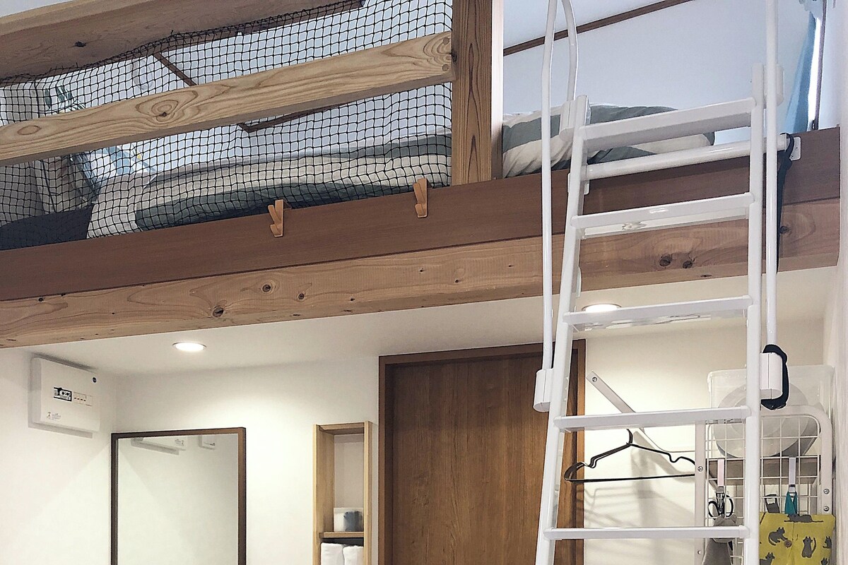Une villa dotée d’une chambre mansardée accessible par une échelle. La salle de bain comprend un lavabo, un miroir et un porte-serviettes.