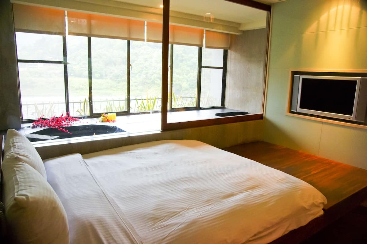 Un dormitorio con una cama grande, un televisor montado en la pared y una ventana con vistas al verdor.