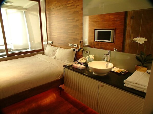 Habitación de hotel con cama, un espejo grande, un lavabo y una televisión.