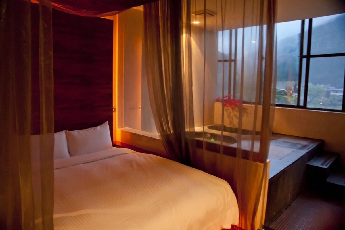 Un dormitorio con cama, ventana y vista a la ciudad.