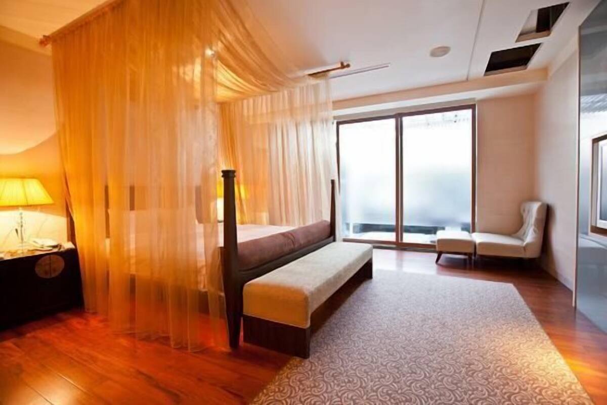 Un dormitorio con cama, banco, mesita de noche y vistas amplias a través de un ventanal.