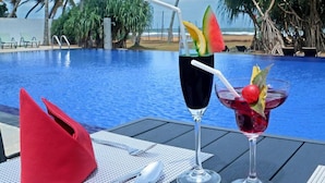 A poolside table with a red napkin, two drinks, and a spoon.