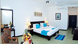 A hotel room with a bed, two bedside tables, a desk with a chair, a fruit basket, and a blue rug.