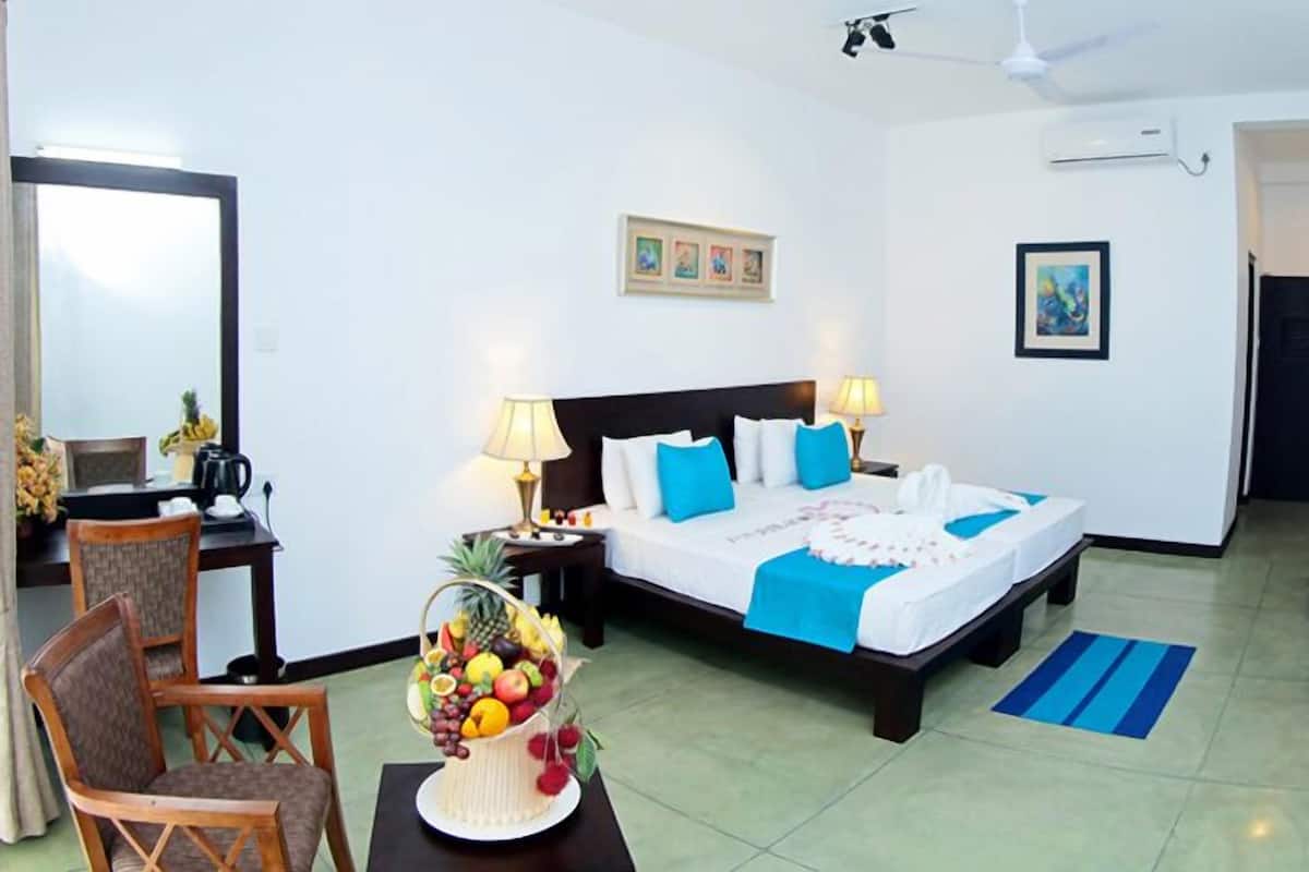 Une chambre d’hôtel avec un lit, deux tables de chevet, un bureau avec une chaise, un panier de fruits et un tapis bleu.