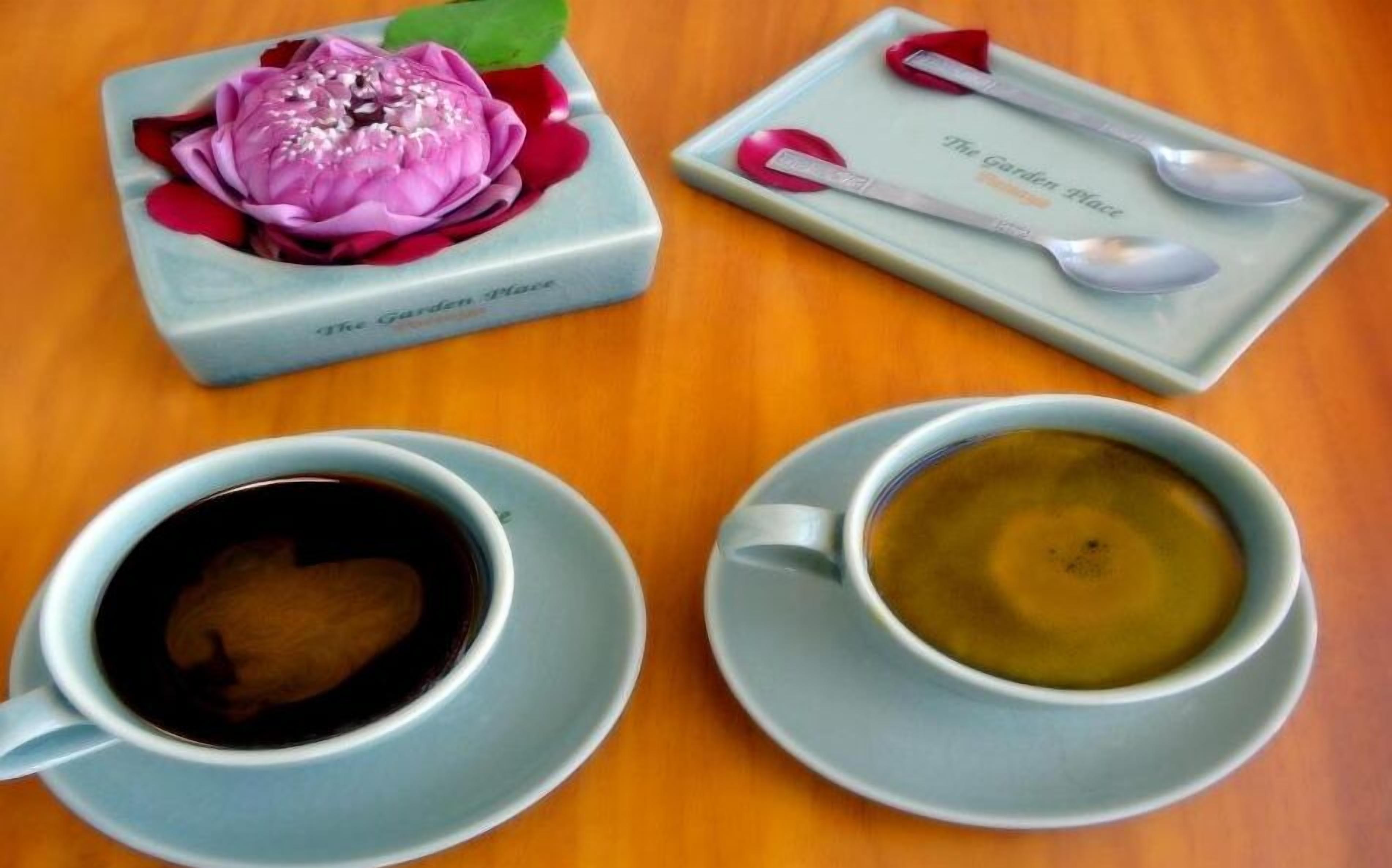 A table with a floral centerpiece, a tray with a spoon and a cup, and two cups of coffee.