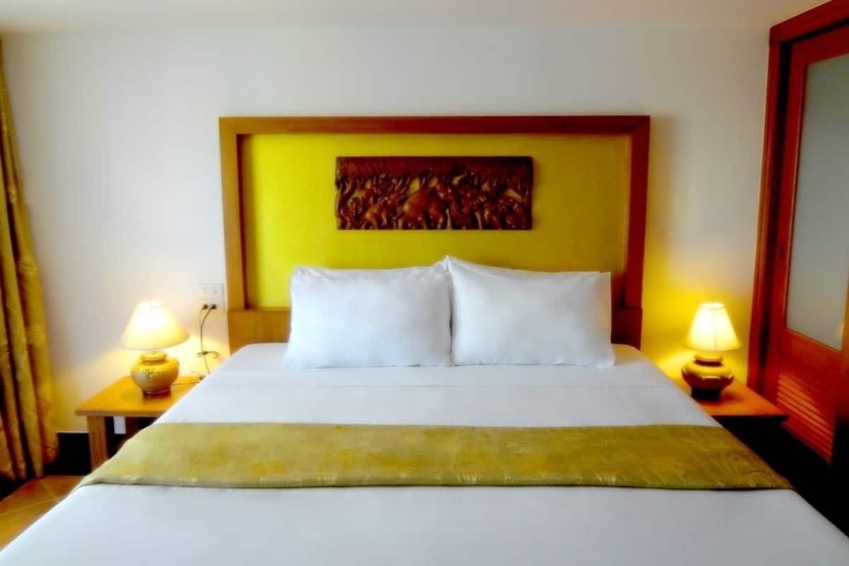 Ein Hotelzimmer mit einem großen Bett, zwei Nachttischlampen, einer gelben Akzentwand und einem gerahmten Kunstwerk darüber.