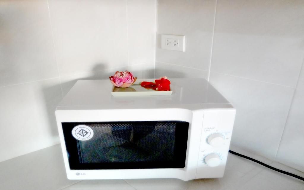Un forno a microonde bianco in un angolo di una stanza con pareti piastrellate bianche e pavimento bianco.