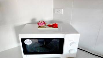 Un forno a microonde bianco in un angolo di una stanza con pareti piastrellate bianche e pavimento bianco.