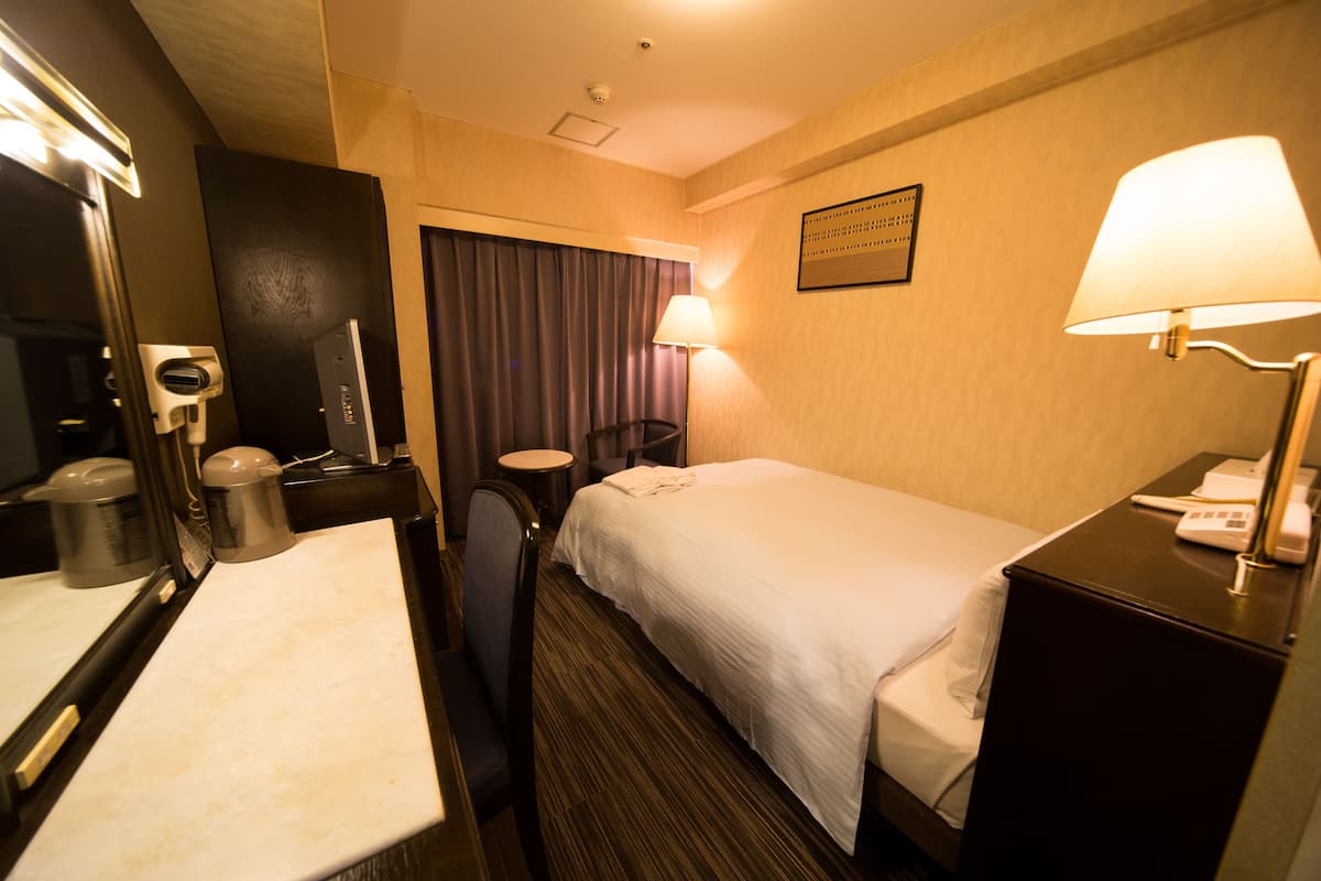 Una habitación de hotel con cama, mesita de noche, lámpara, silla y espejo.