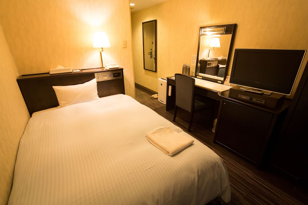 Una habitación de hotel con cama, escritorio, computadora, televisor y espejo.