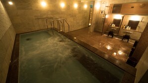 A swimming pool with a glass barrier, a shower area, and a mirror reflecting the room.