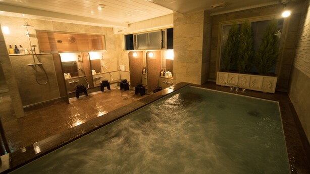 A modern bathroom with a large bathtub, multiple mirrors, and a window with a view of trees.