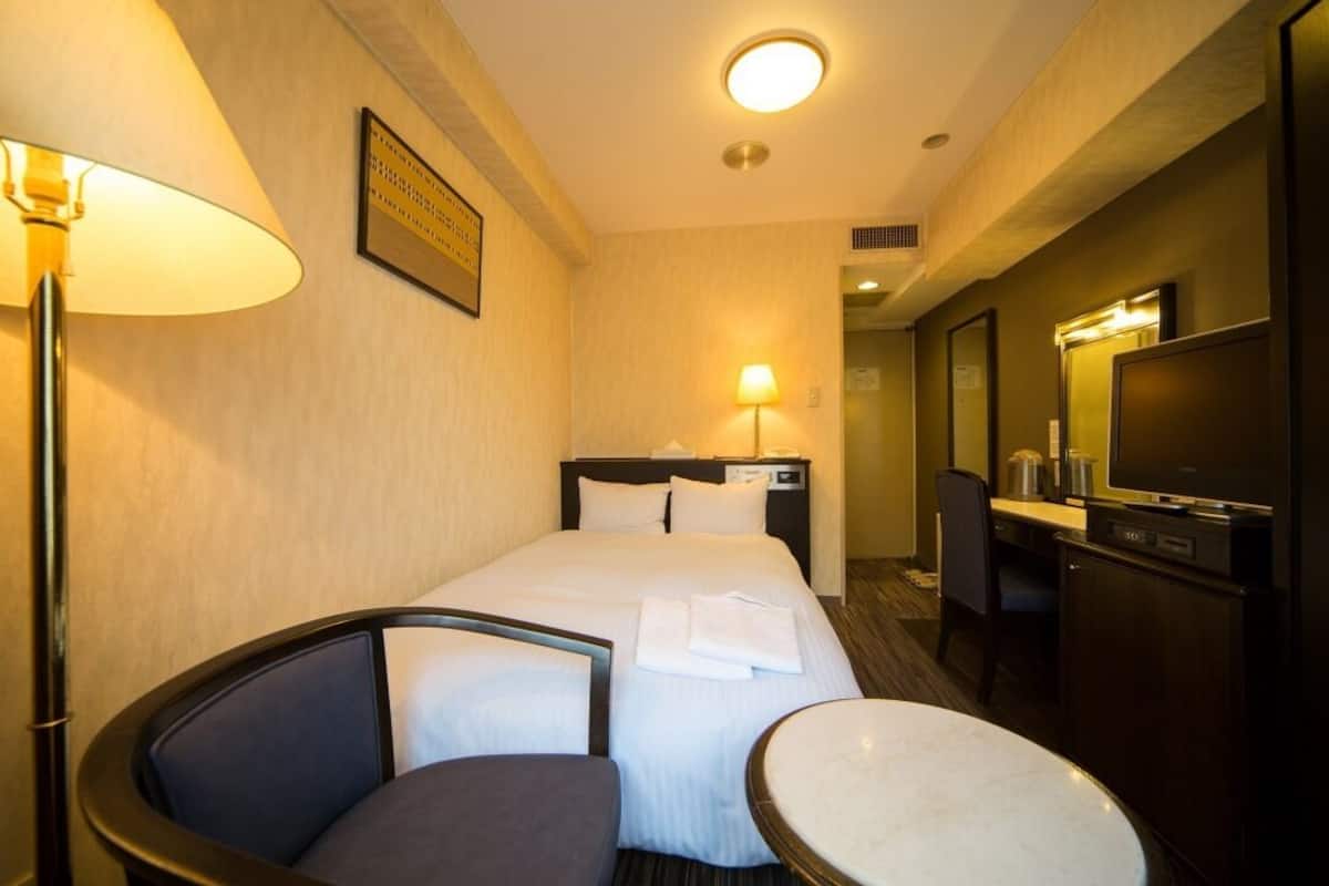 Habitación de hotel con cama, escritorio, silla, una mesita, televisión y lámpara.