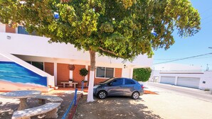 A parking area with a car, a bench, a tree, and a building with a mural. - Playa Azul Kino (Bahía Kino)