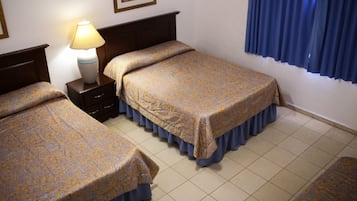 Une chambre d’hôtel avec deux lits, une table de chevet, une lampe, un tableau encadré au mur et une fenêtre avec des rideaux bleus.