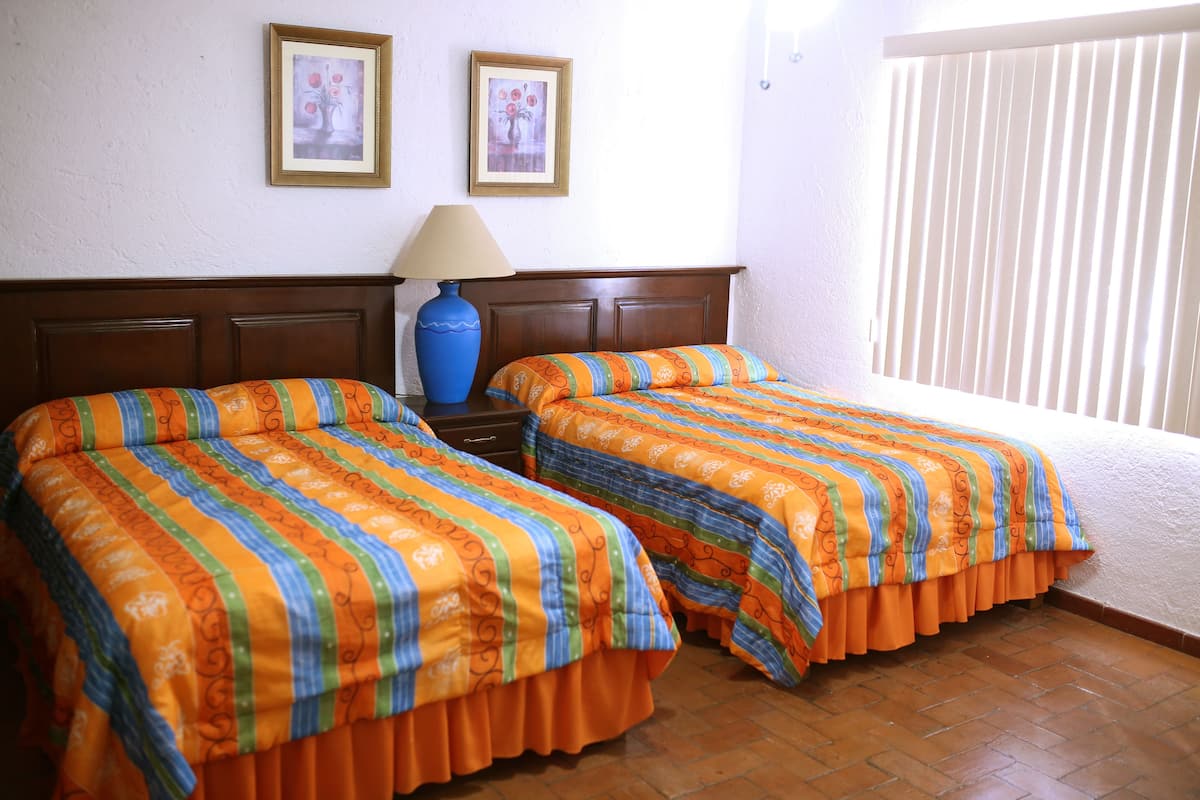 Una habitación con dos camas, una mesita de noche, una lámpara y dos cuadros en la pared.