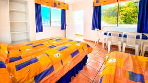 A room with a bed, a desk, and a chair. There are windows with curtains, a ceiling fan, and a view of greenery outside. - Playa Azul Kino (Bahía Kino)