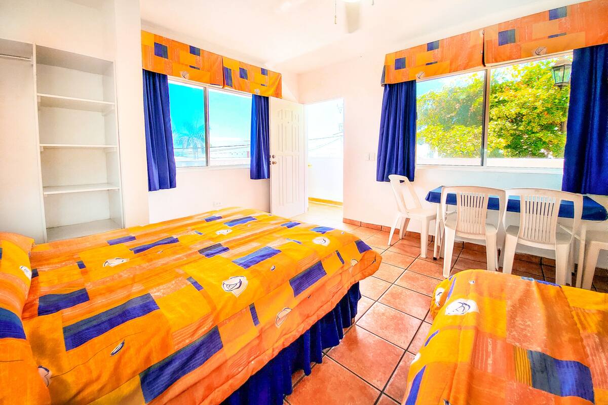 Habitación con cama, escritorio y silla. Ventanas con cortinas, ventilador de techo y vistas al exterior.