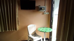 A small room with a single white chair, a green patterned table, a television mounted on the wall, and a power outlet. - M&A Guesthouse (Hua Hin)