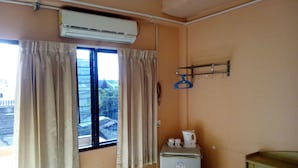 A room with a window, curtains, an air conditioner, a small table with a kettle, and a wall-mounted hanger rack. - M&A Guesthouse (Hua Hin)