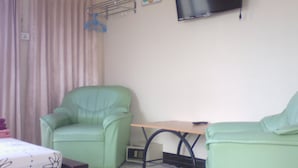 A room with a green armchair, a small table, a television mounted on the wall, and a curtain. - M&A Guesthouse (Hua Hin)