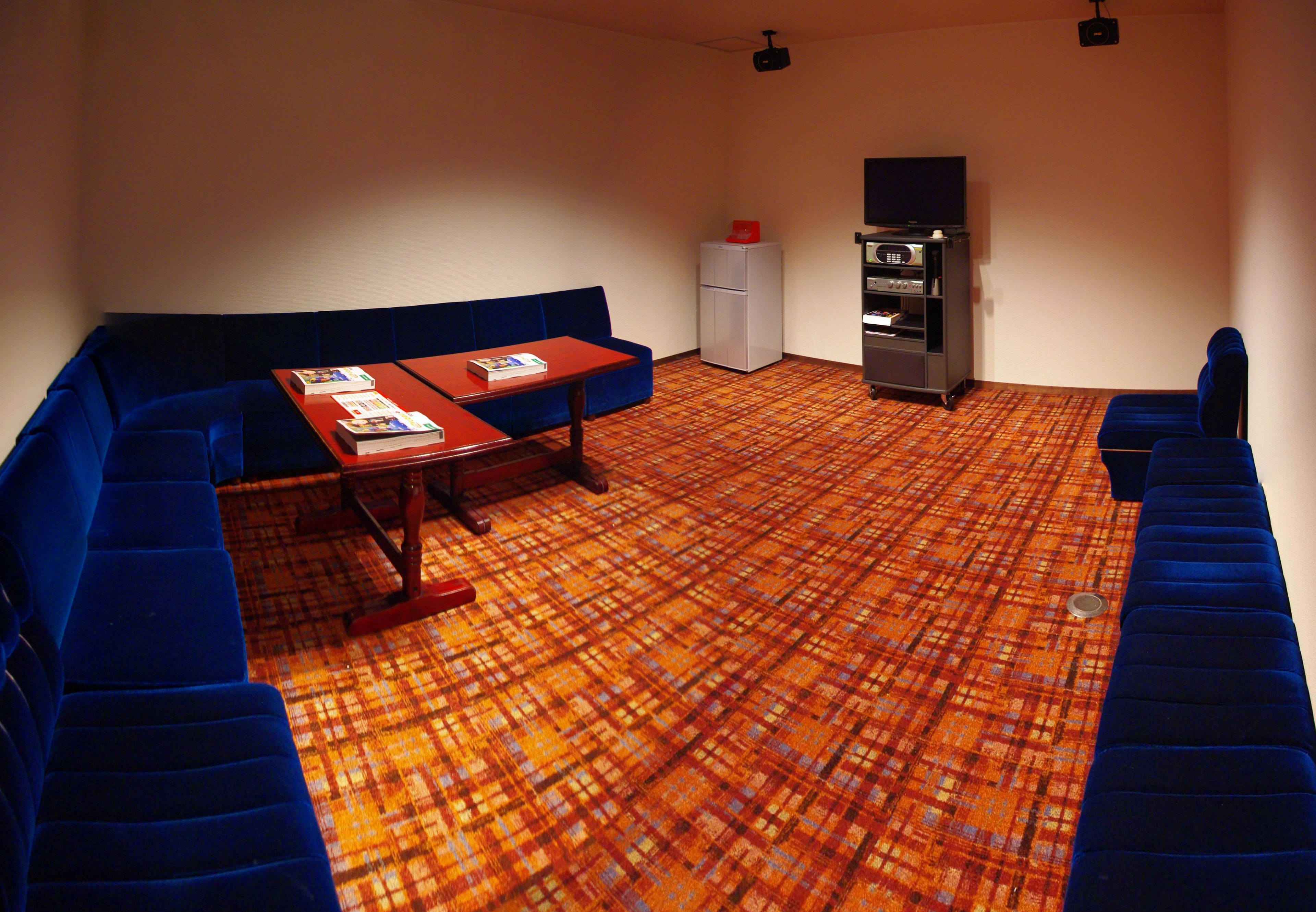 A room with a blue sofa, a small table with a book, a refrigerator, and a TV on a stand.
