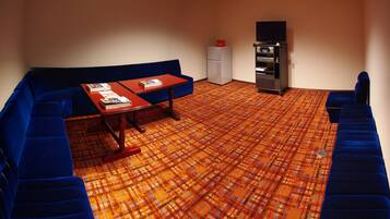 A room with a blue sofa, a small table with a book, a refrigerator, and a TV on a stand.