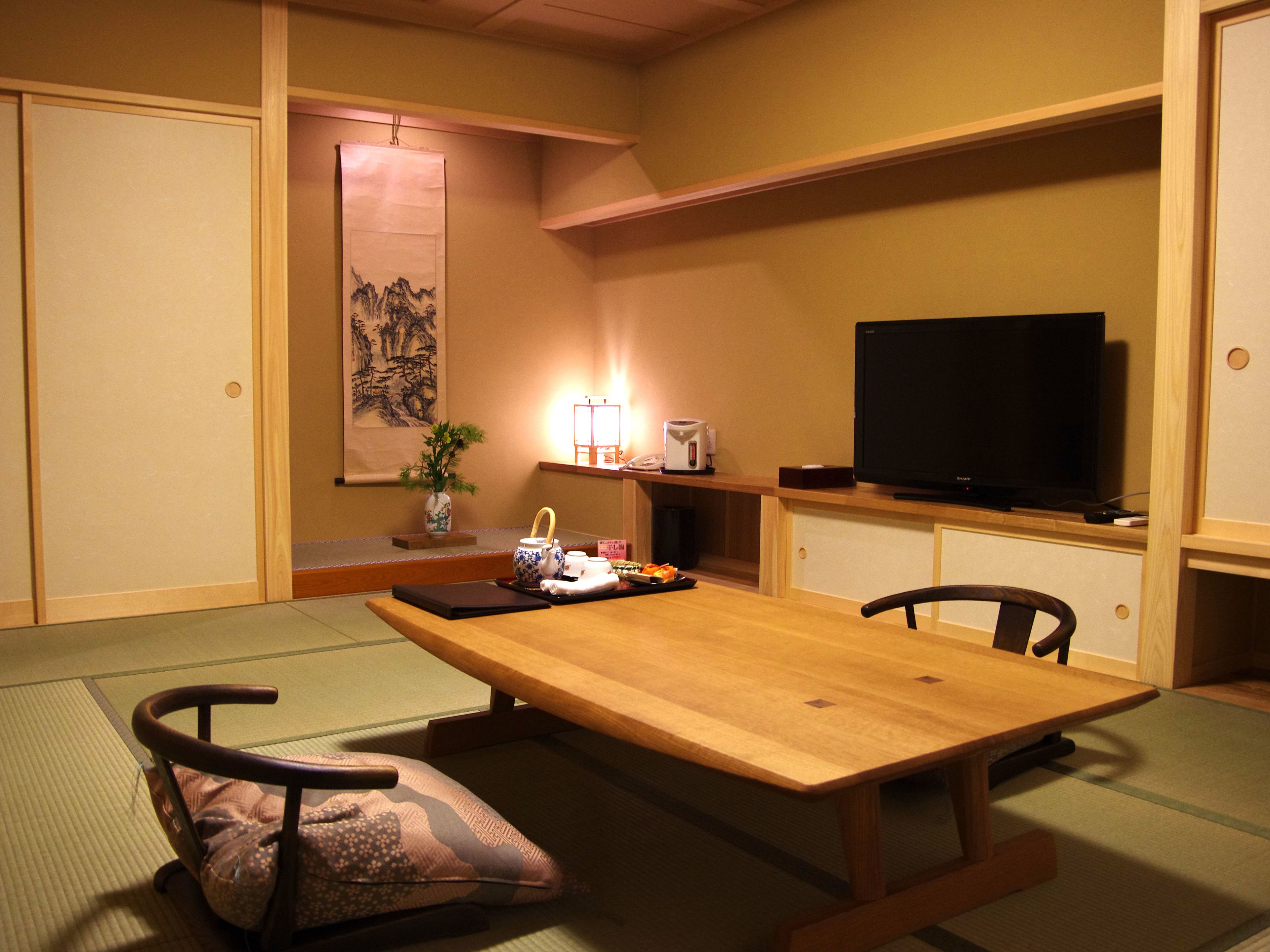 Una habitación japonesa tradicional con suelo de tatami, una mesa de madera baja, un televisor y un estante pequeño con un jarrón y una tetera.