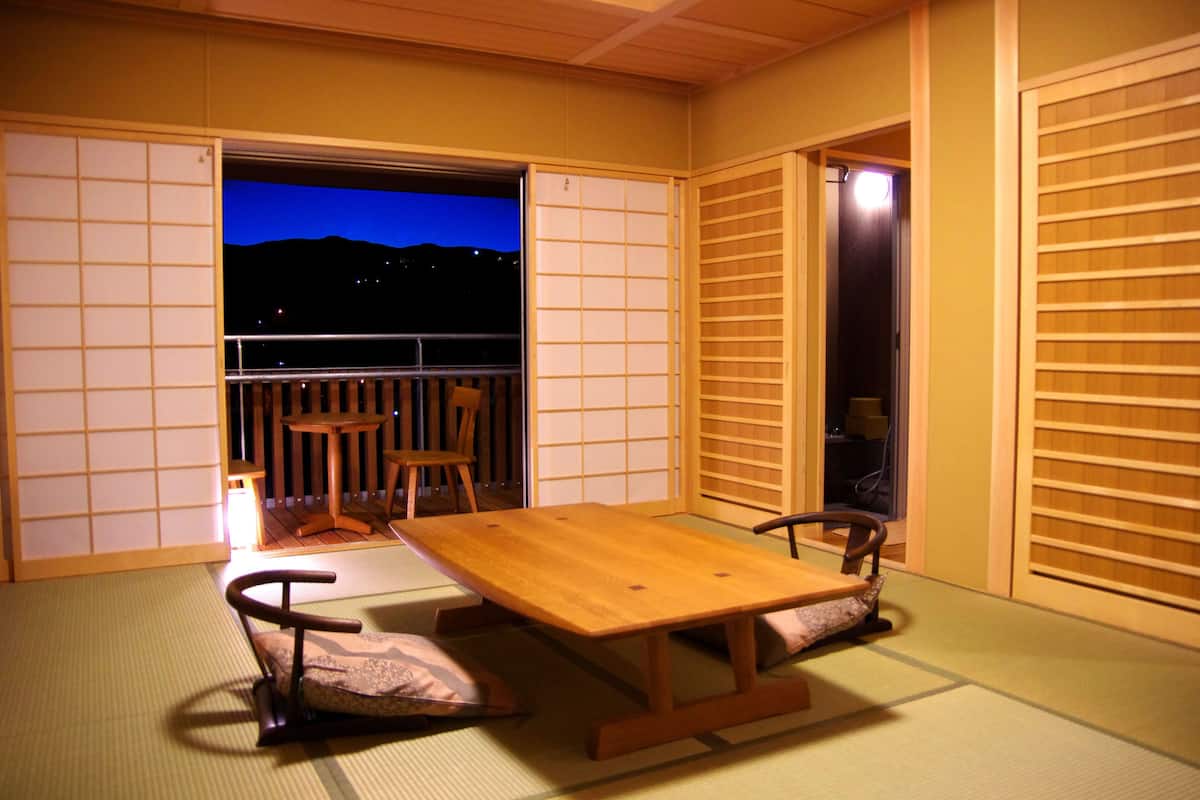Une pièce de style japonais traditionnel, avec un sol recouvert de tatamis, une petite table en bois et une vue sur le ciel nocturne.