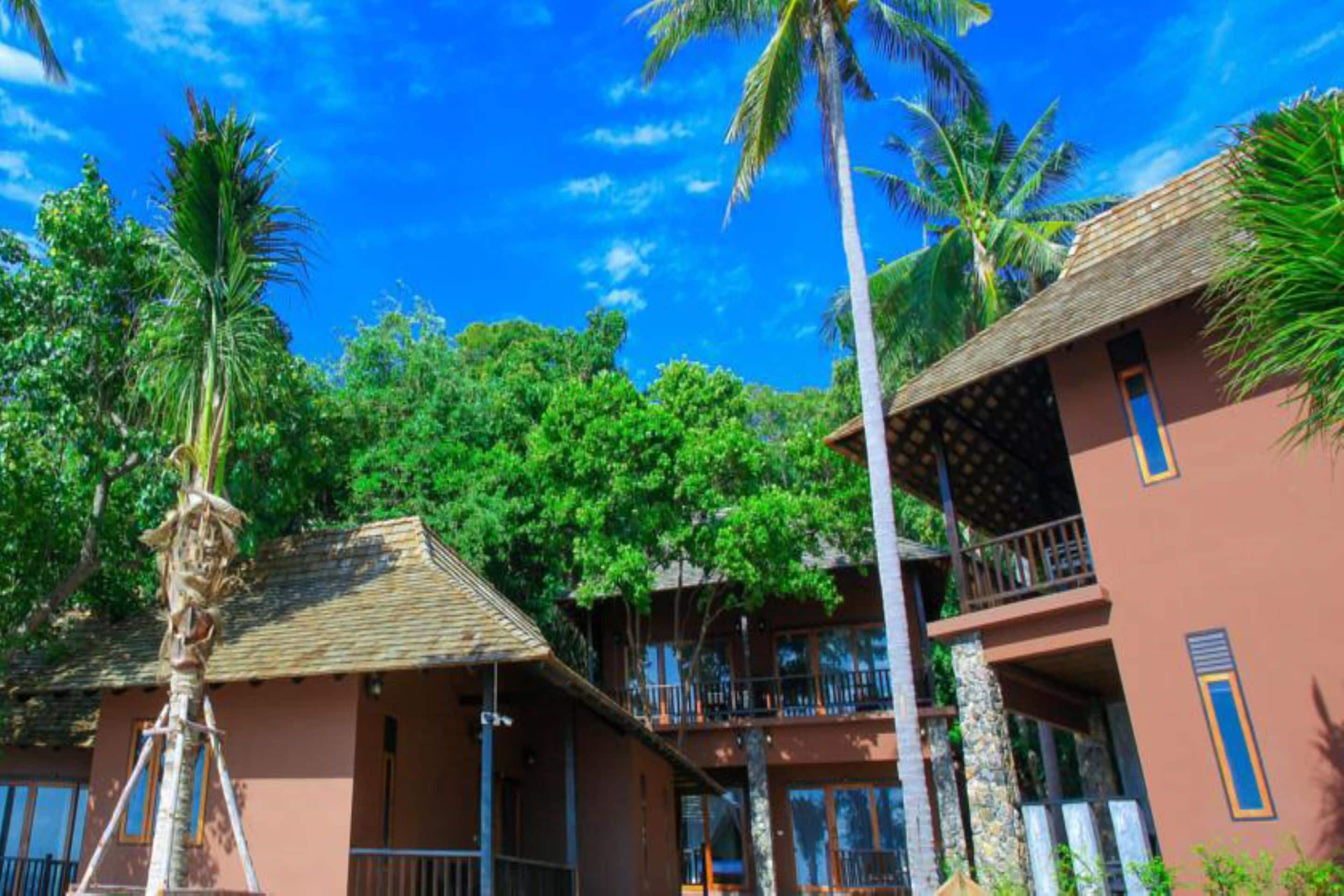 A multi-story building with balconies, surrounded by lush greenery and palm trees.