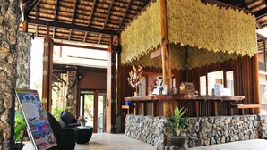 A reception area with a stone wall, a wooden reception desk, and a hanging bamboo decoration. - Koh Tao Beach Club (Koh Tao)