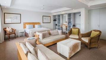 A modern hotel room with a large bed, two sofas, a small table, wicker chairs, and built-in wardrobes.